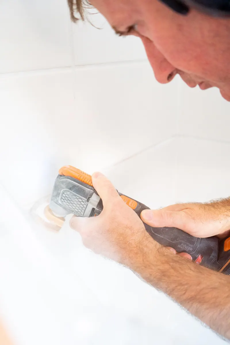 Handwerker entfernt mit dem Multitool alte Fugen im Bad